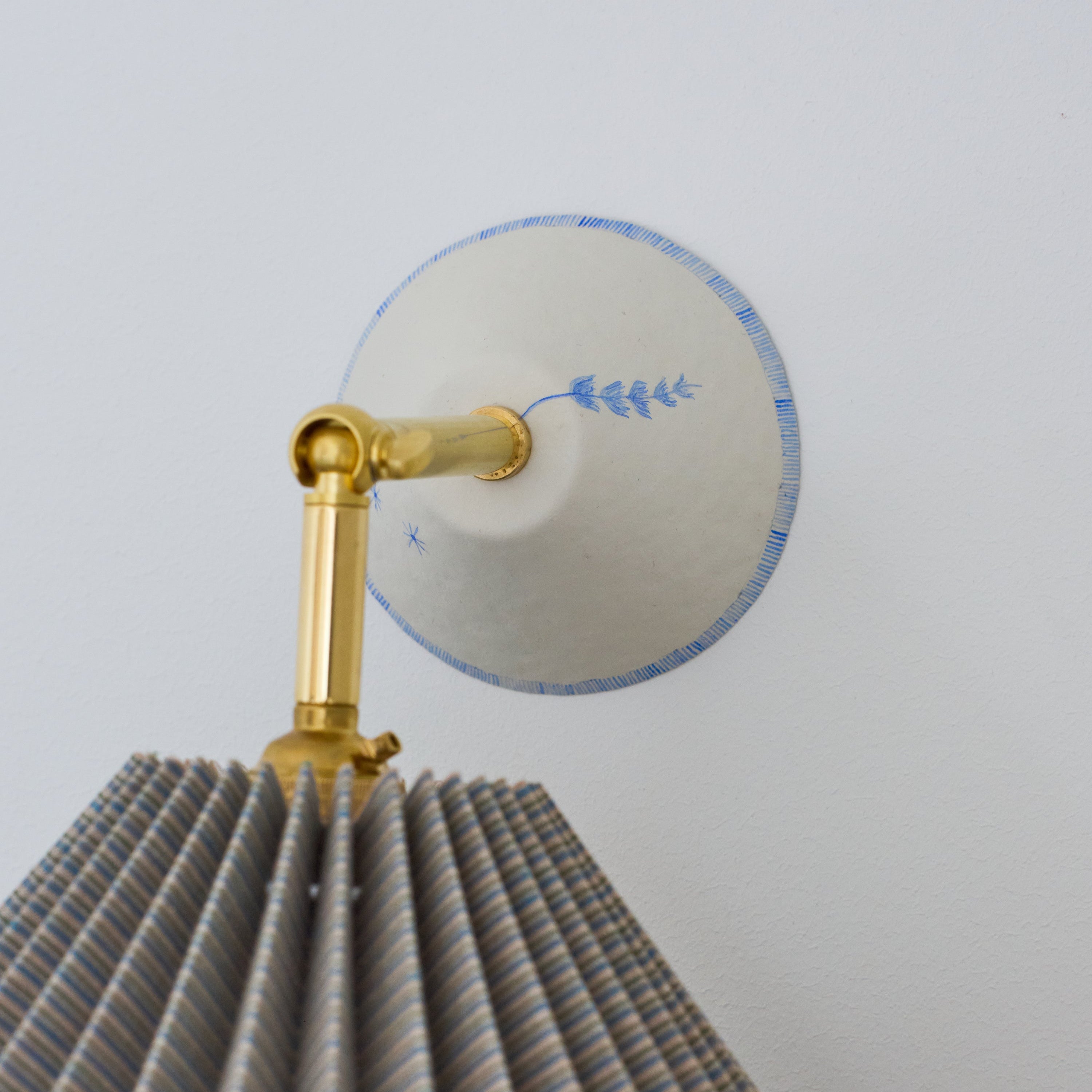 Decorative wall light fixture with pleated design and gold accent on a white background