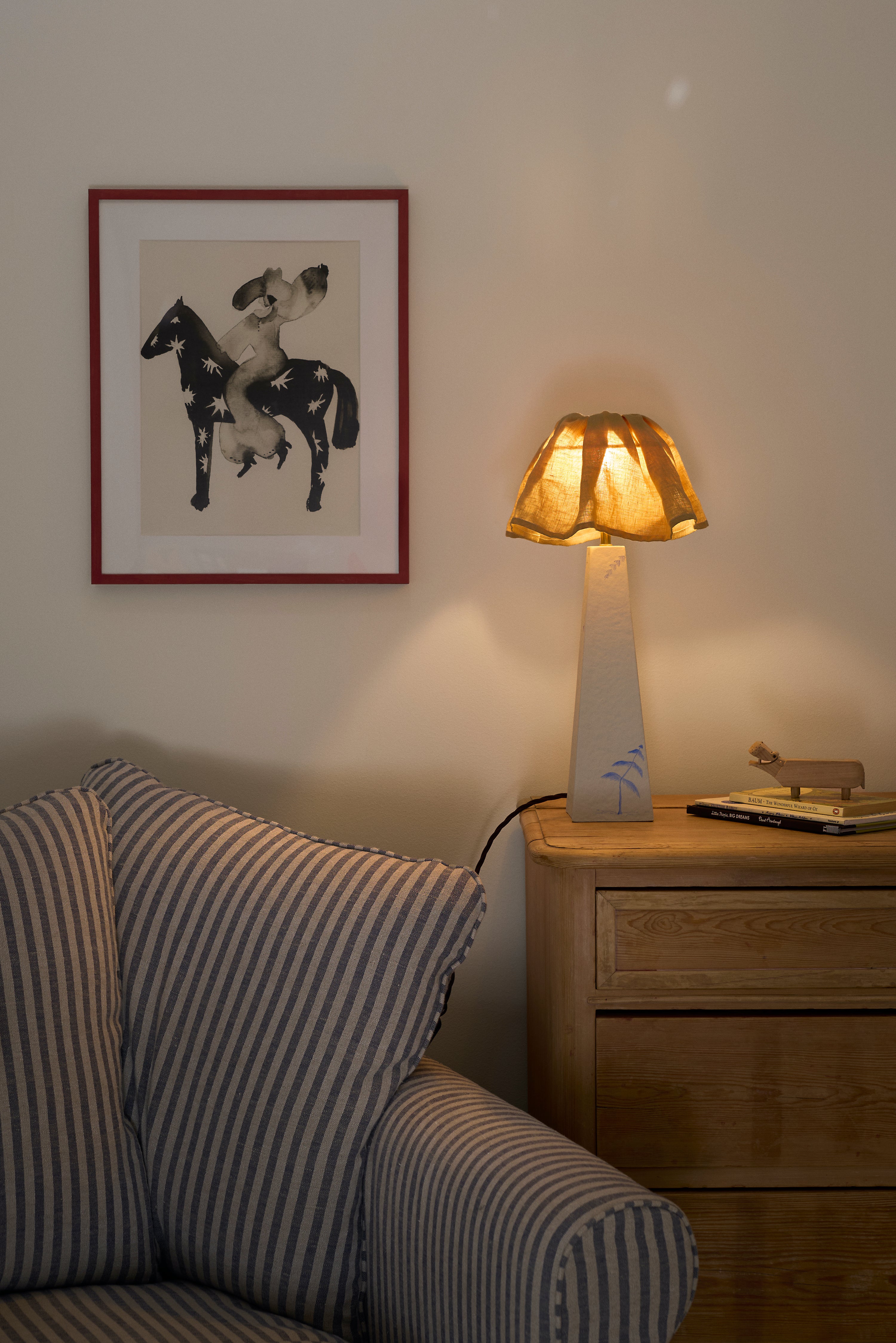 Napoleon on a horse framed picture above a striped sofa with a lamp on a side table.
